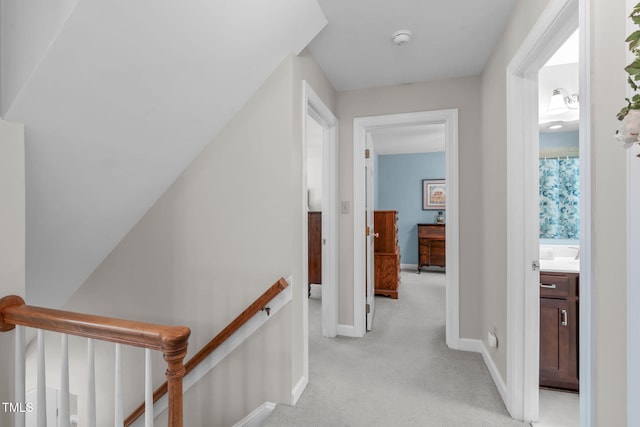 corridor featuring an upstairs landing, light colored carpet, and baseboards