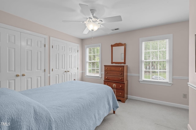 bedroom featuring two closets, baseboards, light colored carpet, and a ceiling fan
