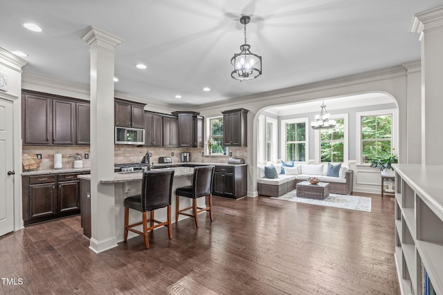 3304 Rockland Ridge Dr, Cary, NC 27519 - kitchen with stainless steel microwave, arched walkways, a chandelier, dark brown cabinetry, and ornamental molding
