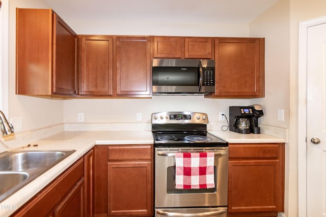 kitchen with a sink, appliances with stainless steel finishes, brown cabinets, and light countertops