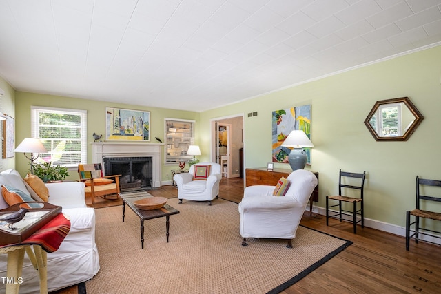 living area with visible vents, crown molding, wood finished floors, baseboards, and a fireplace with flush hearth