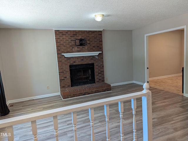 unfurnished living room with a brick fireplace, a textured ceiling, baseboards, and wood finished floors