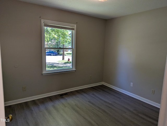 empty room with dark wood-style flooring, baseboards, and visible vents