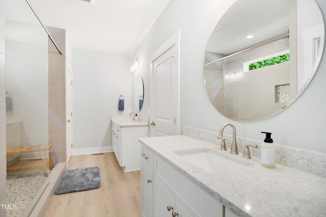 full bath featuring a sink, walk in shower, wood finished floors, and two vanities