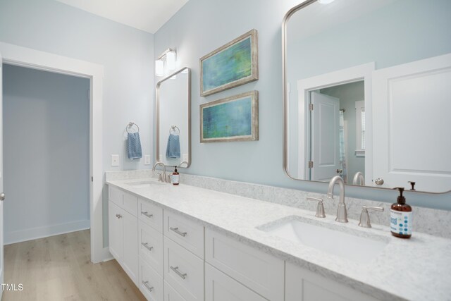 full bath with a sink, double vanity, and wood finished floors