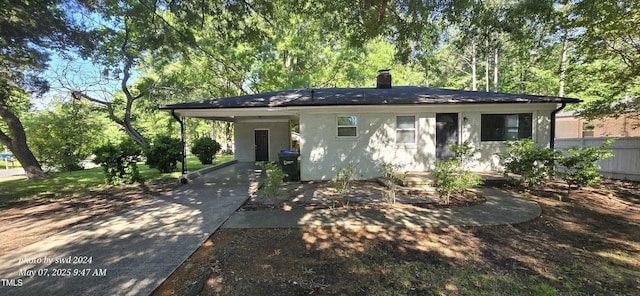 view of front of property featuring driveway, a carport, a chimney, fence, and stucco siding