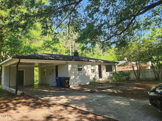 view of front of house featuring concrete driveway, an attached carport, fence, and a chimney