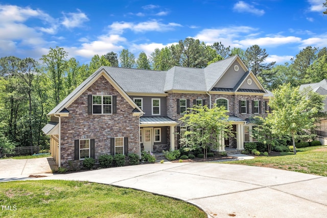 view of front of house with covered porch, a standing seam roof, a front yard, fence, and stone siding