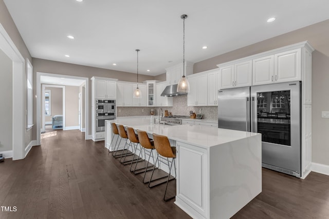 kitchen with appliances with stainless steel finishes, dark wood finished floors, wall chimney exhaust hood, white cabinetry, and decorative backsplash