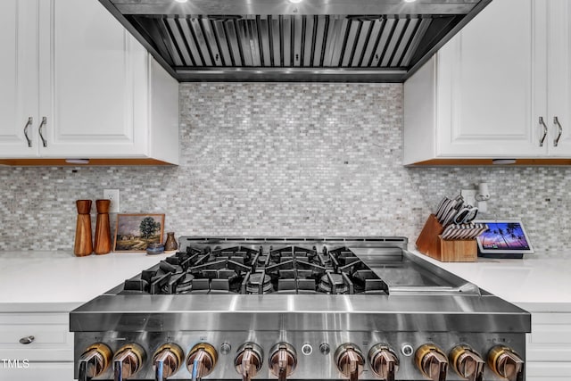 kitchen with stove, wall chimney range hood, light countertops, white cabinets, and backsplash
