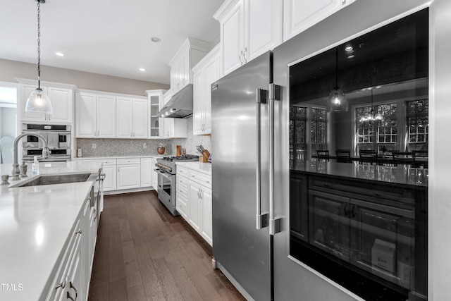 kitchen with white cabinets, high quality appliances, dark wood finished floors, backsplash, and under cabinet range hood