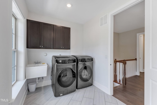 laundry room featuring cabinet space, a sink, light wood-style floors, visible vents, and washer and clothes dryer