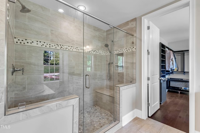 bathroom featuring wood finished floors, baseboards, a stall shower, and a spacious closet