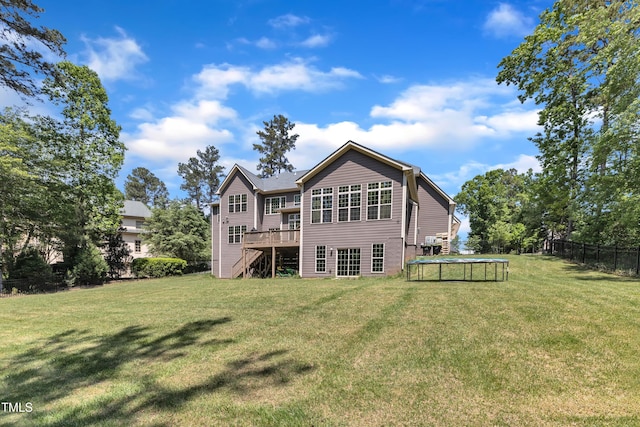 rear view of house with fence, a trampoline, a wooden deck, stairway, and a lawn
