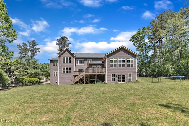 back of property featuring a lawn, a wooden deck, stairs, and a trampoline