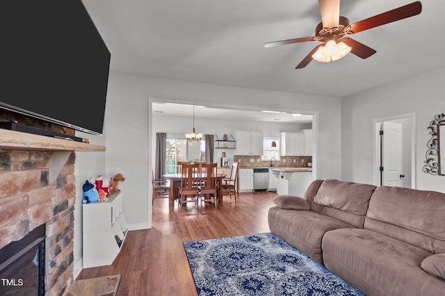living room featuring baseboards, a stone fireplace, ceiling fan with notable chandelier, and wood finished floors