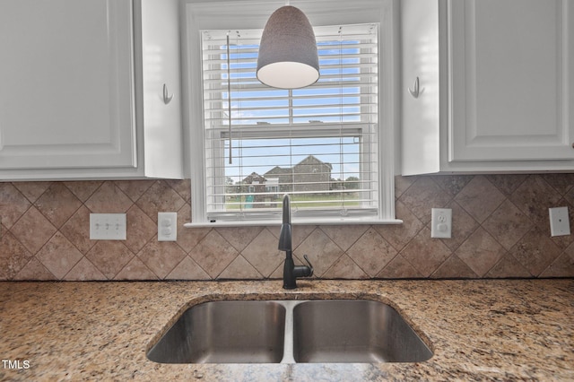 interior details featuring light stone counters, a sink, white cabinetry, and decorative backsplash