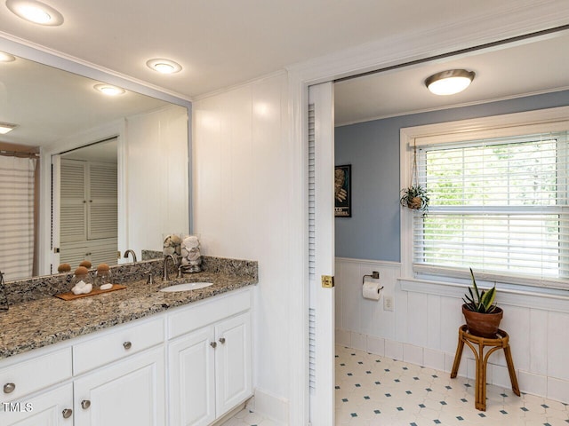 bathroom with wainscoting, a decorative wall, vanity, tile patterned floors, and baseboards