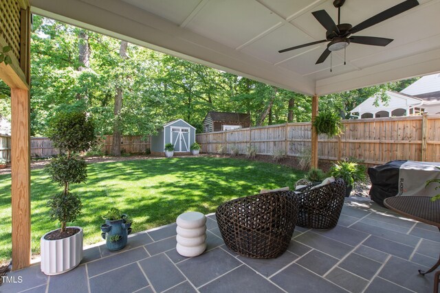 view of patio / terrace with an outdoor structure, ceiling fan, a fenced backyard, and a shed