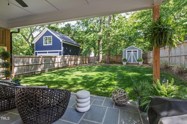 view of yard with a storage shed, a fenced backyard, an outbuilding, a ceiling fan, and a patio