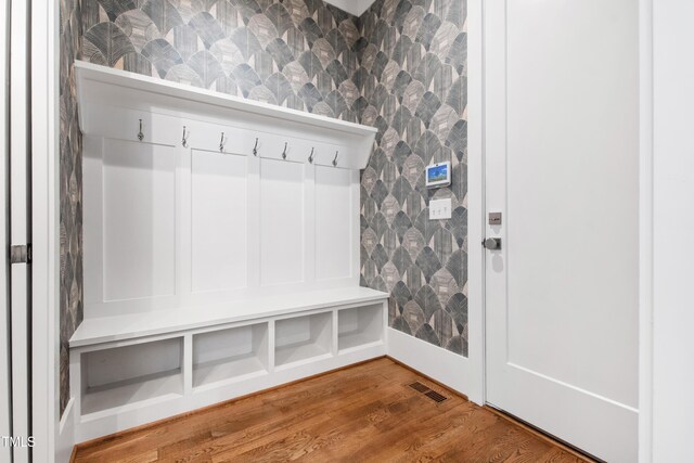 mudroom with visible vents, wood finished floors, and wallpapered walls