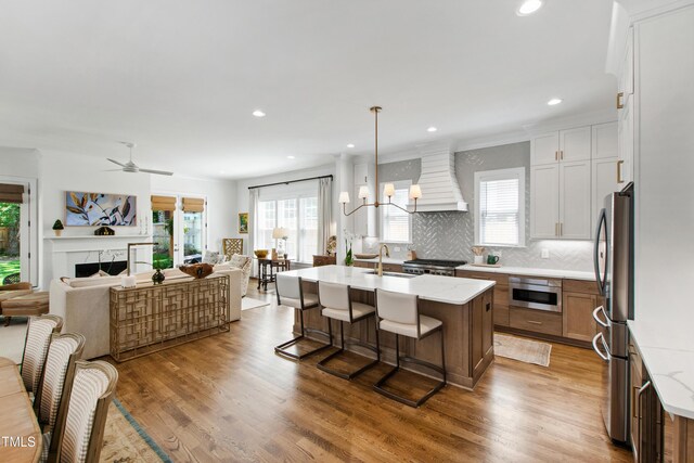 kitchen with a sink, freestanding refrigerator, custom exhaust hood, open floor plan, and a breakfast bar