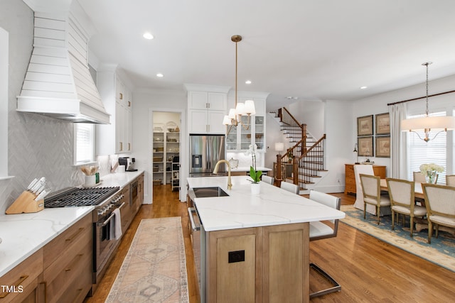 kitchen with appliances with stainless steel finishes, a sink, light wood-style floors, custom range hood, and backsplash