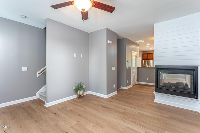8719 Cypress Grove Run, Raleigh, NC 27612 - unfurnished living room with ceiling fan, light wood-style flooring, stairs, a multi sided fireplace, and baseboards