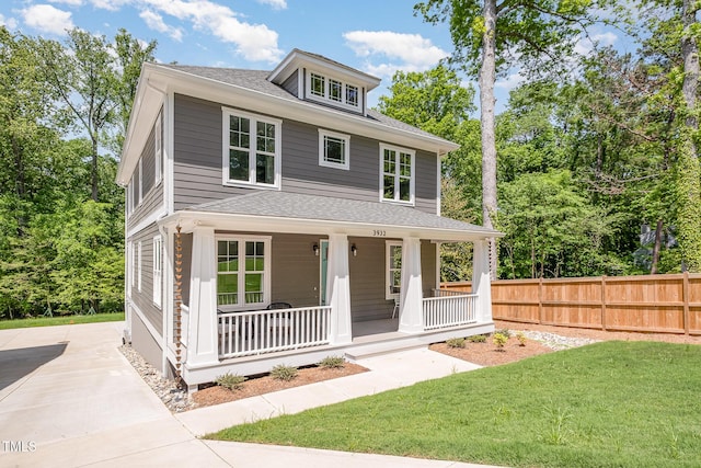 traditional style home featuring covered porch, fence, a shingled roof, and a front yard