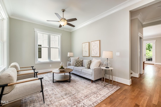 living area with baseboards, ornamental molding, a ceiling fan, and wood finished floors