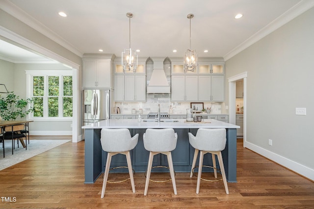 kitchen with backsplash, a center island with sink, light countertops, baseboards, and custom exhaust hood