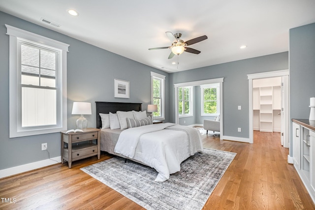 bedroom featuring baseboards, visible vents, a walk in closet, and light wood finished floors