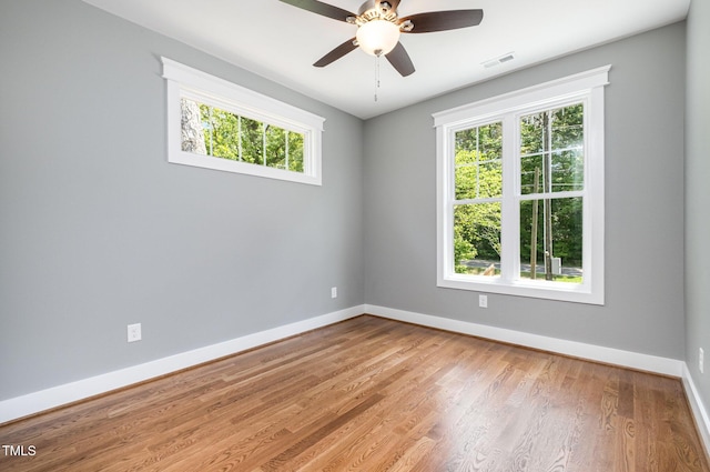 empty room with baseboards, a ceiling fan, wood finished floors, and visible vents