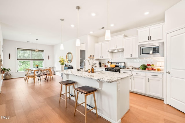 2404 Azalea Dr, Durham, NC 27703 - kitchen with appliances with stainless steel finishes, under cabinet range hood, a sink, decorative backsplash, and light wood finished floors