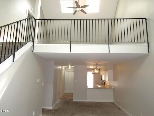 interior space with baseboards, a ceiling fan, a towering ceiling, and carpet floors