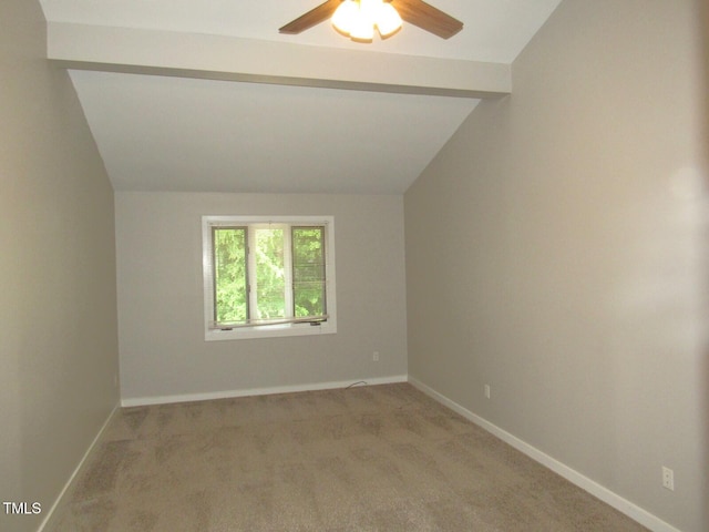 empty room with light colored carpet, a ceiling fan, lofted ceiling with beams, and baseboards