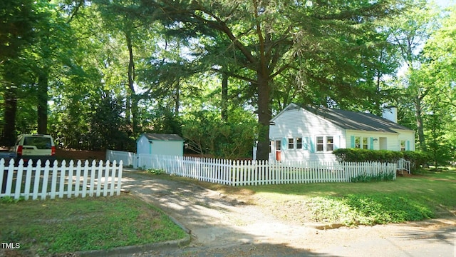 view of side of property with a fenced front yard, a shed, a chimney, an outdoor structure, and driveway