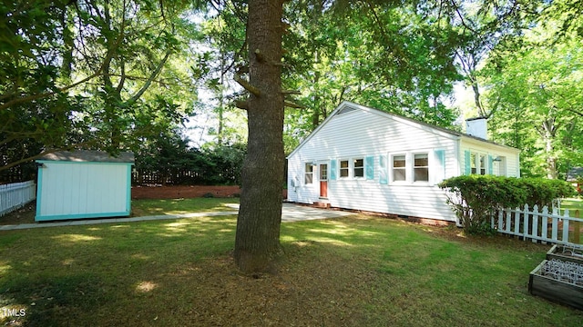 back of property featuring a chimney, a lawn, fence, an outdoor structure, and a shed
