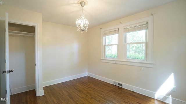 unfurnished bedroom featuring a closet, visible vents, baseboards, dark wood-style floors, and a notable chandelier