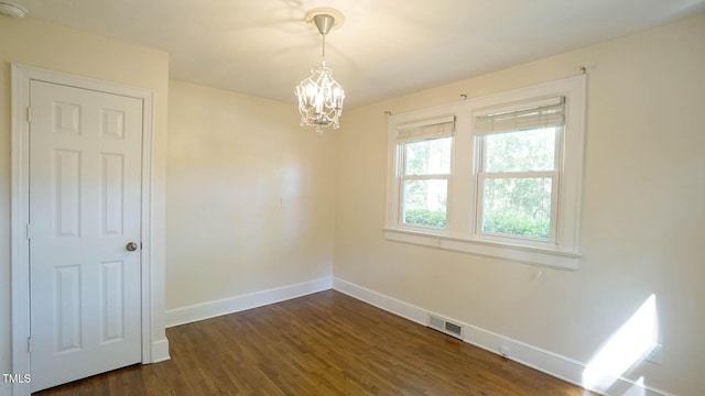 spare room with baseboards, dark wood-style flooring, a notable chandelier, and visible vents