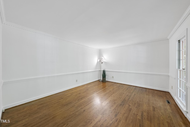 spare room with crown molding, baseboards, wood finished floors, and visible vents
