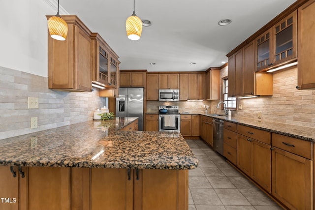 128 Cobblestone Dr, Chapel Hill, NC 27516 - kitchen featuring appliances with stainless steel finishes, brown cabinets, a peninsula, light tile patterned flooring, and dark stone countertops