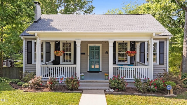 bungalow-style home with a porch, a chimney, a shingled roof, and a front yard
