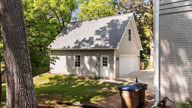 view of side of home featuring roof with shingles, a detached garage, an outdoor structure, and a lawn