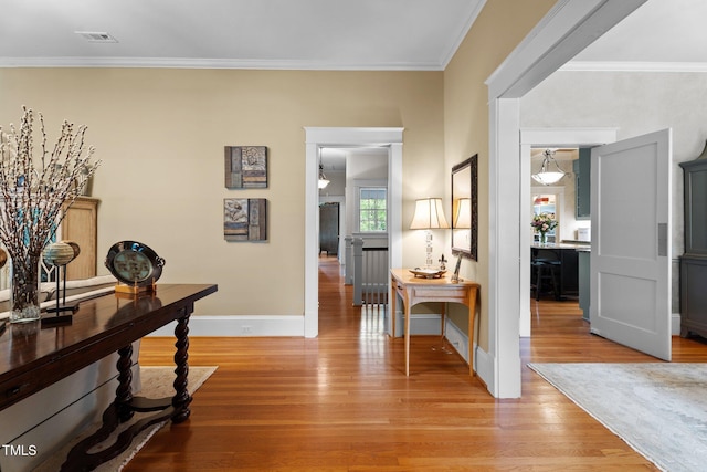 hall featuring baseboards, visible vents, ornamental molding, and light wood finished floors
