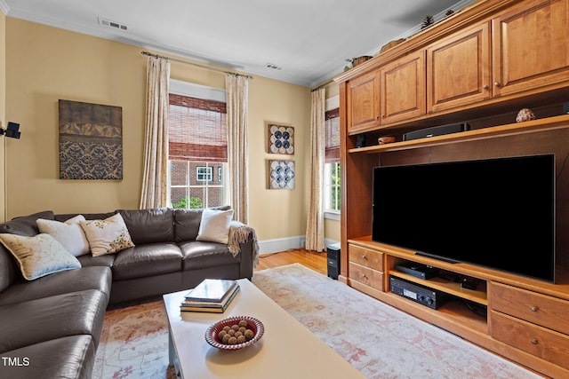 living room with baseboards, visible vents, ornamental molding, and light wood-style floors