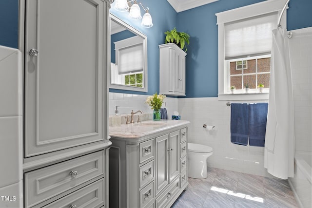 bathroom featuring vanity, toilet, a chandelier, a wainscoted wall, and tile walls
