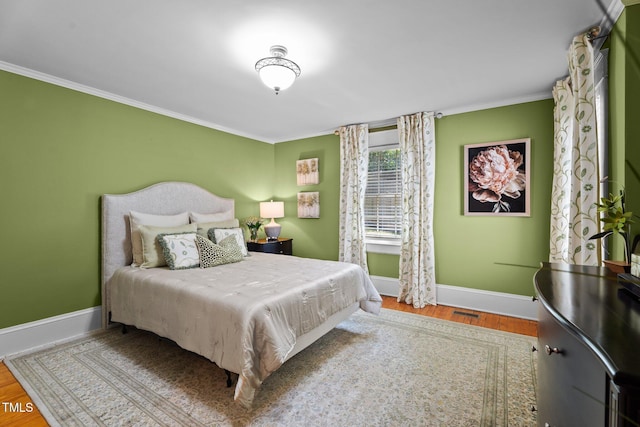 bedroom with baseboards, ornamental molding, wood finished floors, and visible vents