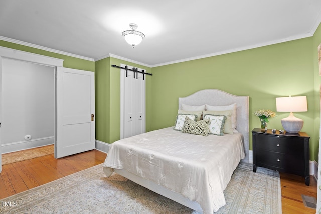 bedroom featuring ornamental molding, a closet, a barn door, and wood finished floors