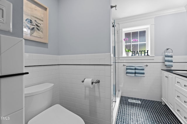 full bath featuring a tile shower, vanity, toilet, a wainscoted wall, and tile walls